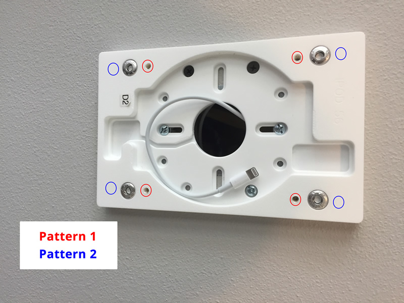 Mounting bracket for electronic device on wall with labeled screw positions for Pattern 1 and Pattern 2 installations, showing circular cutout and white cable.