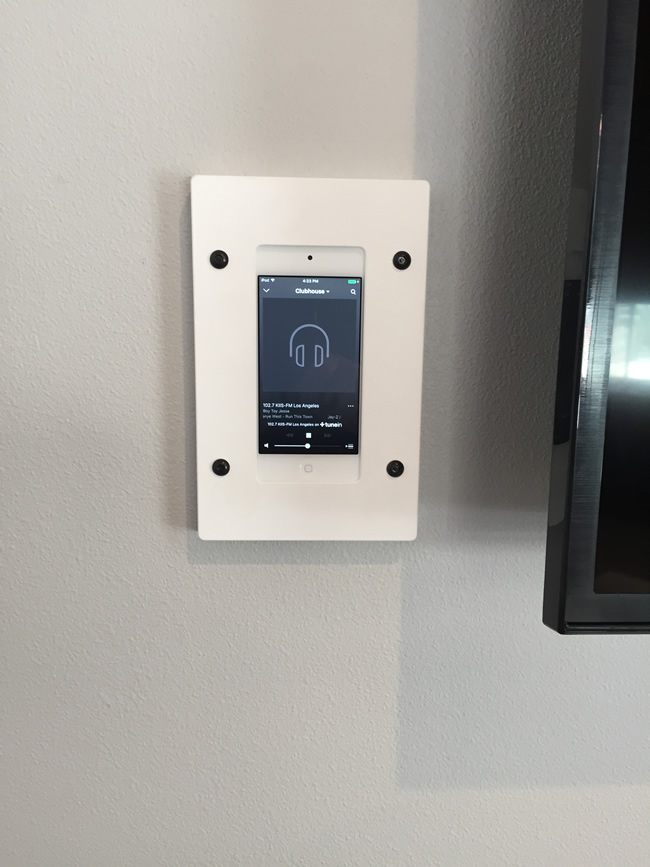 Wall-mounted white electronic device playing a radio station.